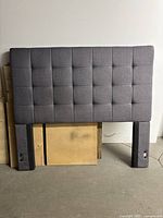 Full front view of the gray fabric upholstered headboard showing grid stitch pattern and attached legs.