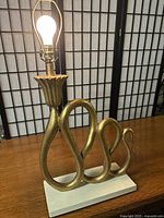 Front view of the lamp showing the gold snake-inspired sculptural body and white base with a light bulb attached, no shade.