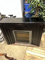 Front view of the electric fireplace showing black wood frame and glass front with imitation logs.