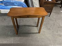 Front view of a light brown wooden table showing rectangular top with curved edges and single drawer with wooden knob.