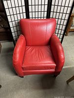 Front view of the red leather armchair showing seat cushion, backrest, and armrests with minor wear and creasing.
