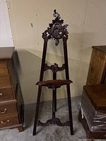 Full front view of easel showing carved top, adjustable shelf, and base