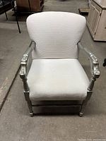 Full front view of armchair showing white textured upholstery and carved floral details on silver armrests and legs.