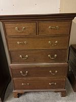 Front view of wooden chest showing six drawers with brass handles and crown molding top.