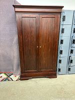 Closed view of wooden armoire showing cherry finish, double paneled doors, and classic molding.
