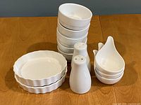 Stack of miniature round pie plates, condiment bowls, and salt & pepper shakers on wooden table