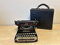 Typewriter unfolded next to closed carrying case on tabletop