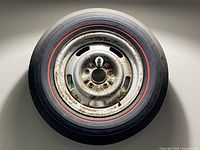 Top view of 1967 Corvette spare tire mounted on steel rally wheel showing tire red stripe and wheel surface rust.