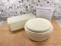 Three vintage plastic storage containers on cork mat with tile backsplash, showing all three containers grouped together.