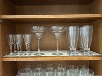Photo of 3 types of bar glasses arranged on shelf: 6 sherry/champagne flutes on left, 2 margarita/daiquiri glasses center, 4 tall beer ale glasses on right.