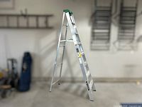 Full view of the 8ft aluminum step ladder standing open in a garage, showing green top step and six steps on silver aluminum frame.
