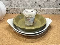 Three ceramic baking pie plates stacked, with a container of ceramic pie weights on top.