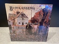 Front cover of Black Sabbath 1970 vinyl LP in original shrink wrap showing artwork of house and figure in woods.