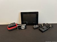 Canon PowerShot A2600 camera, red carrying case, Canadian and European battery chargers, and Aluratek digital photo frame on display.