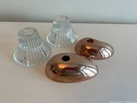 Two pink metal candle holders and two clear ribbed glass candle holders placed on a white surface.