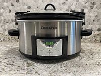 Front view of the Crock-Pot Original Slow Cooker showing stainless steel body with black handles and digital control panel illuminated with a timer.