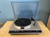 Front view of turntable with dust cover open, showing metal plinth, black platter mat and tonearm