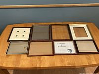Top view of eight picture and certificate frames arranged on a wooden table showing front sides and frame styles.