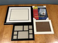 Four picture frames on table: two black frames and two white frames. One frame is new in package.