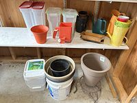 Front view of all garden supplies on a shelf showing containers, pots, watering cans, buckets, and seed spreader.