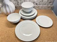 Stack of white ceramic dinner plates, salad plates, and three cereal bowls alongside a decorative white pitcher