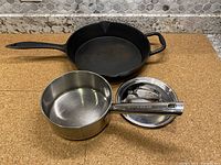 Cast iron frying pan alongside stainless steel saucepan and lid on counter.