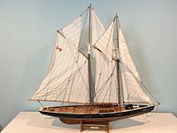 Front angled view of large Bluenose schooner model ship with sails rigged, showing black hull, wooden deck, and Canadian flag on sail.