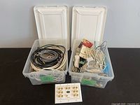 Two plastic storage containers filled with various cables and cords with white lids open showing contents.