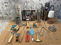 Photo of full lot showing assorted barware and kitchen utensils arranged on cork surface with backdrop of kitchen backsplash.