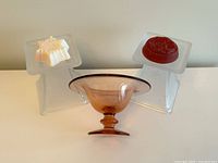 Pink glass dish centered with two frosted square glass pillar candle holders with snowflake patterns on each side, with wax candles on top.