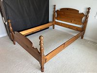 Solid pine queen-size poster bed frame assembled without mattress, showcasing headboard with curved top and cannonball finials on posts, side rails and footboard.