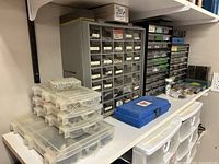 Shelf with multiple plastic drawer organizers, small parts bins, and hardware cases shown from one angle.