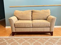 Front view of tan brown two seater sofa, showing fabric upholstery and dark wood legs on hardwood floor, neutral background