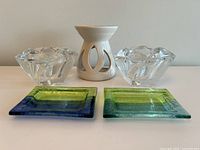 View of two clear star-shaped glass votive candle holders, white ceramic tealight wax warmer, and two blue-green ceramic plates