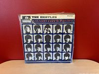 Front cover of The Beatles 1964 UK mono vinyl record 'A Hard Day's Night' in sleeve with plastic cover showing Beatles portraits grid on blue background.