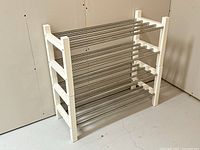 Side angled view showing one shoe rack with white wooden frame and two tiers of stainless steel rods