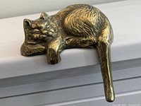 Top-down angled view of the cat sitting on a shelf edge highlighting the extended tail hanging down.