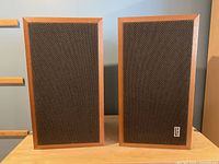 Front view of two PSB speakers with walnut cabinets and black woven fabric grilles on front, one showing a PSB logo.