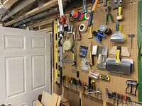 View of workshop tools on pegboard showing rulers, screwdrivers, putty knives, trowels, painting rollers, tapes, and other hand tools organized neatly.