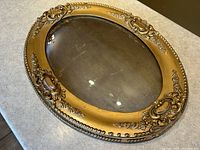 Top-down view showing convex bubble glass and ornate gesso decoration on gold oval frame.
