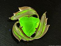 Brooch under UV light showing bright green glow from uranium glass stone and leaf shaped gold metal setting.