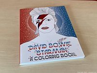Front cover of the David Bowie Starman coloring book featuring stylized iconography of Bowie with lightning bolt face paint on a red and blue starry backdrop.