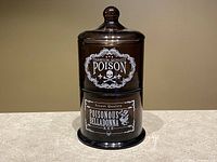 Stacked set of three brown glass jars with white vintage poison-themed labels for decorative purposes.
