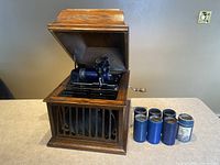 Front left view of phonograph with lid open and seven cylinder records displayed to right