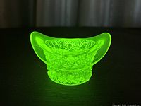 Fenton uranium vaseline glass top hat toothpick holder glowing bright green under blacklight showing detailed Daisy and Button pressed glass pattern.
