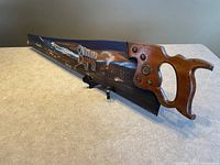 Side angle showing the wooden handle and the painted metal saw blade with a western scene