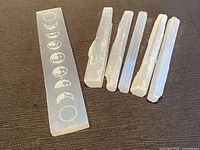 Photo showing flat selenite moon phase healing wand alongside five raw selenite crystal sticks.