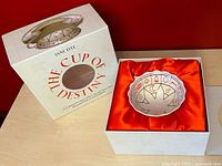 Box set with porcelain cup visible through the round window in the top inside an orange satin lining.