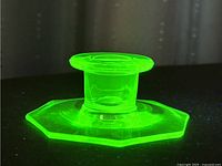 Top-down view of the candlestick holder glowing bright green under black light showing the octagonal base and cylindrical stem.