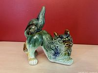 Side view of vintage Chinese porcelain Foo Dog statue showing crouching stance, curled tail, and color variations in green, blue, and tan glaze.